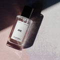 Perfume bottle labeled 'AME' on a textured surface with soft lighting