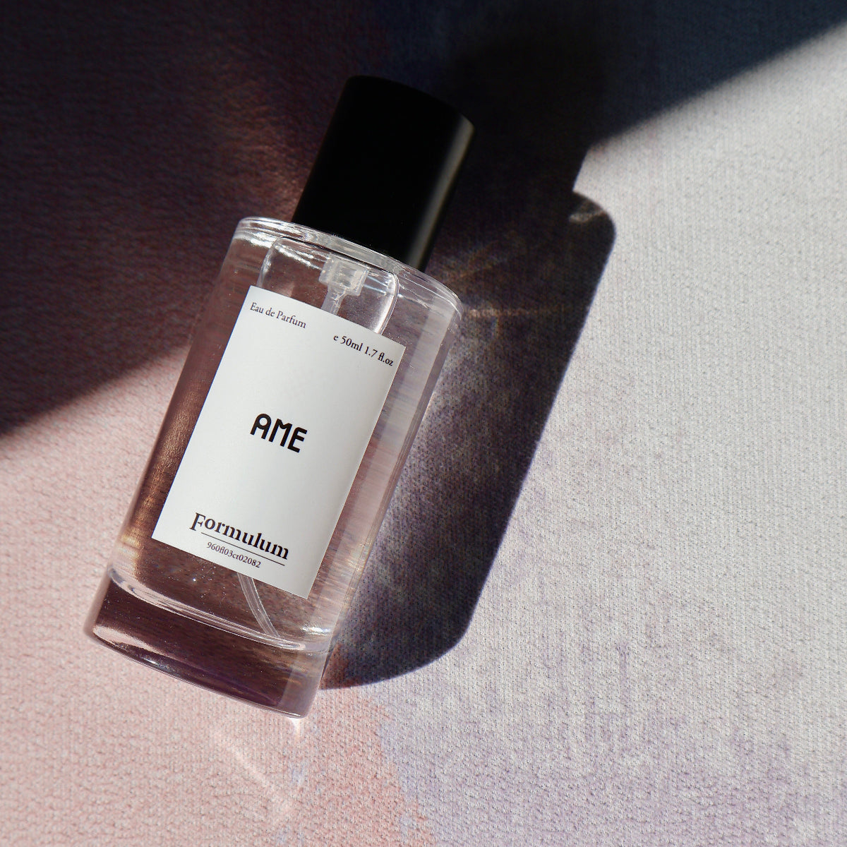 Perfume bottle labeled 'AME' on a textured surface with soft lighting