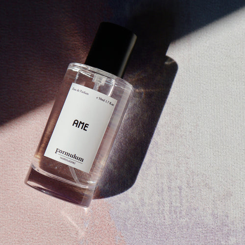 Perfume bottle labeled 'AME' on a textured surface with soft lighting